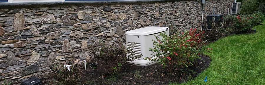 A Generator placed near a stone wall in corner of a garden at Blairstown, NJ